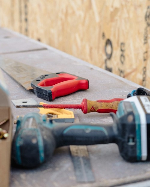 Illustration: a cordless drill, a saw and a screwdriver on a site bench.